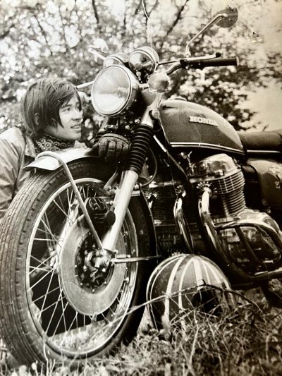 Détective privé caché derrière sa moto lors d'une filature. Photo noir et blanc des années 70.